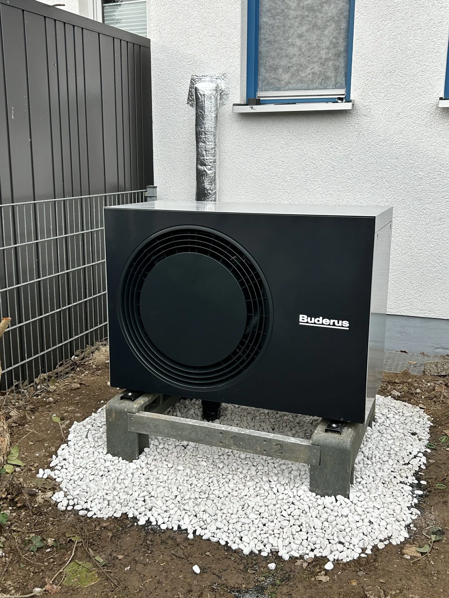 Buderus-Wärmepumpe als Außeneinheit auf Betonsockel an einem Neubau