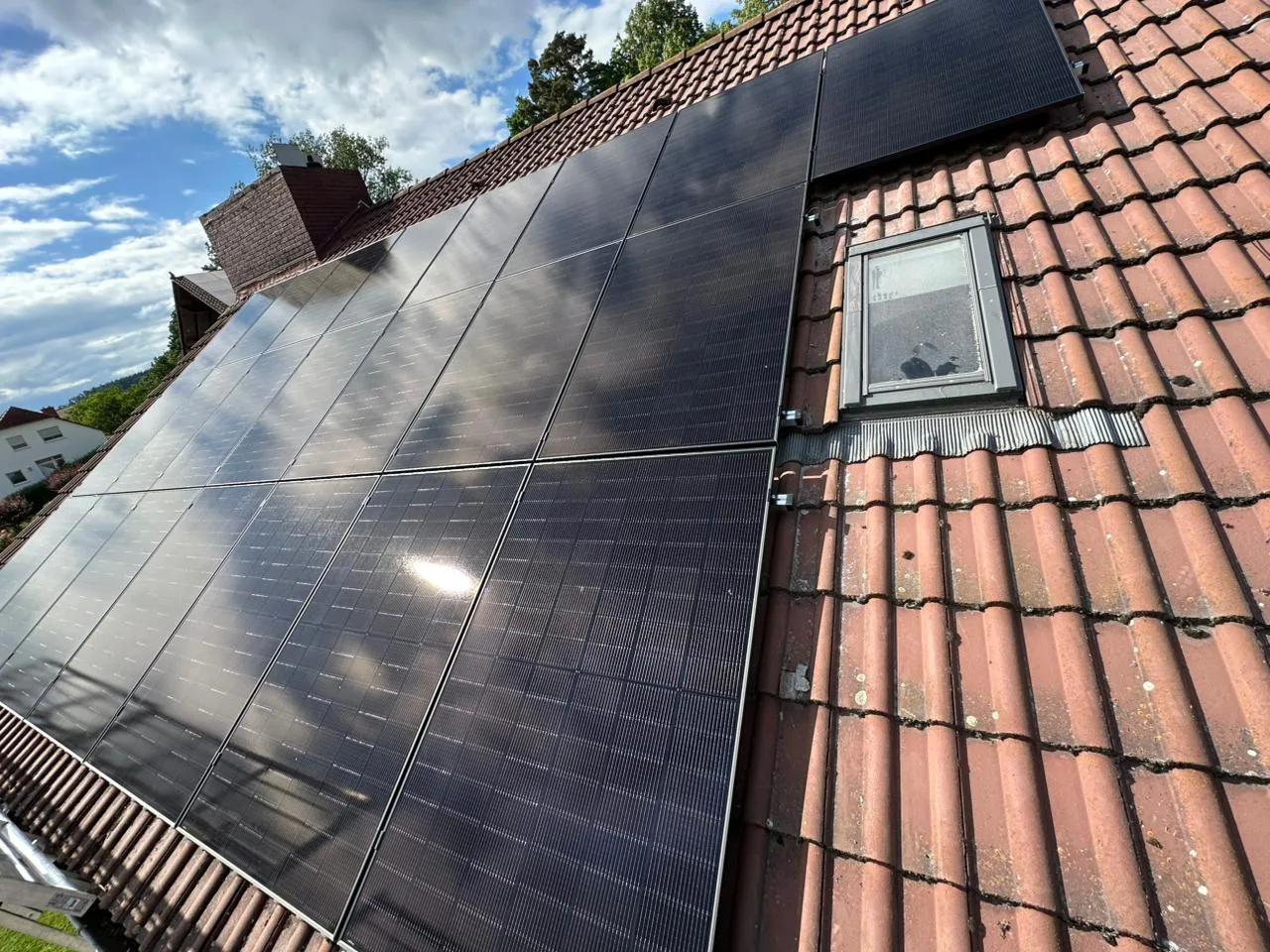 Solarmodule auf rotem Ziegeldach, um ein vorhandenes Dachfenster herum geplant