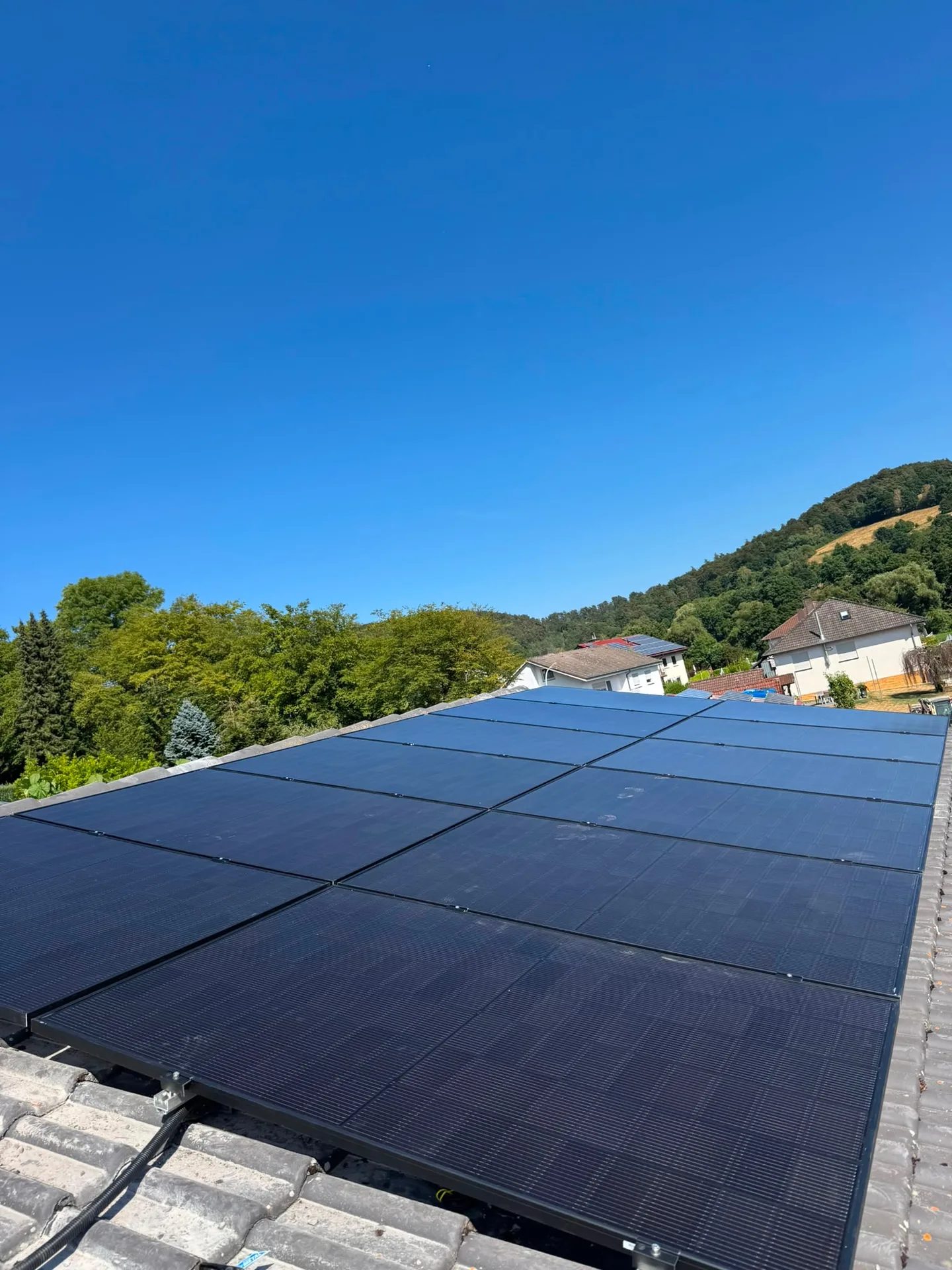 Vollflächig belegtes Ziegeldach mit schwarzen Solarmodulen, Blick über das Fuldatal