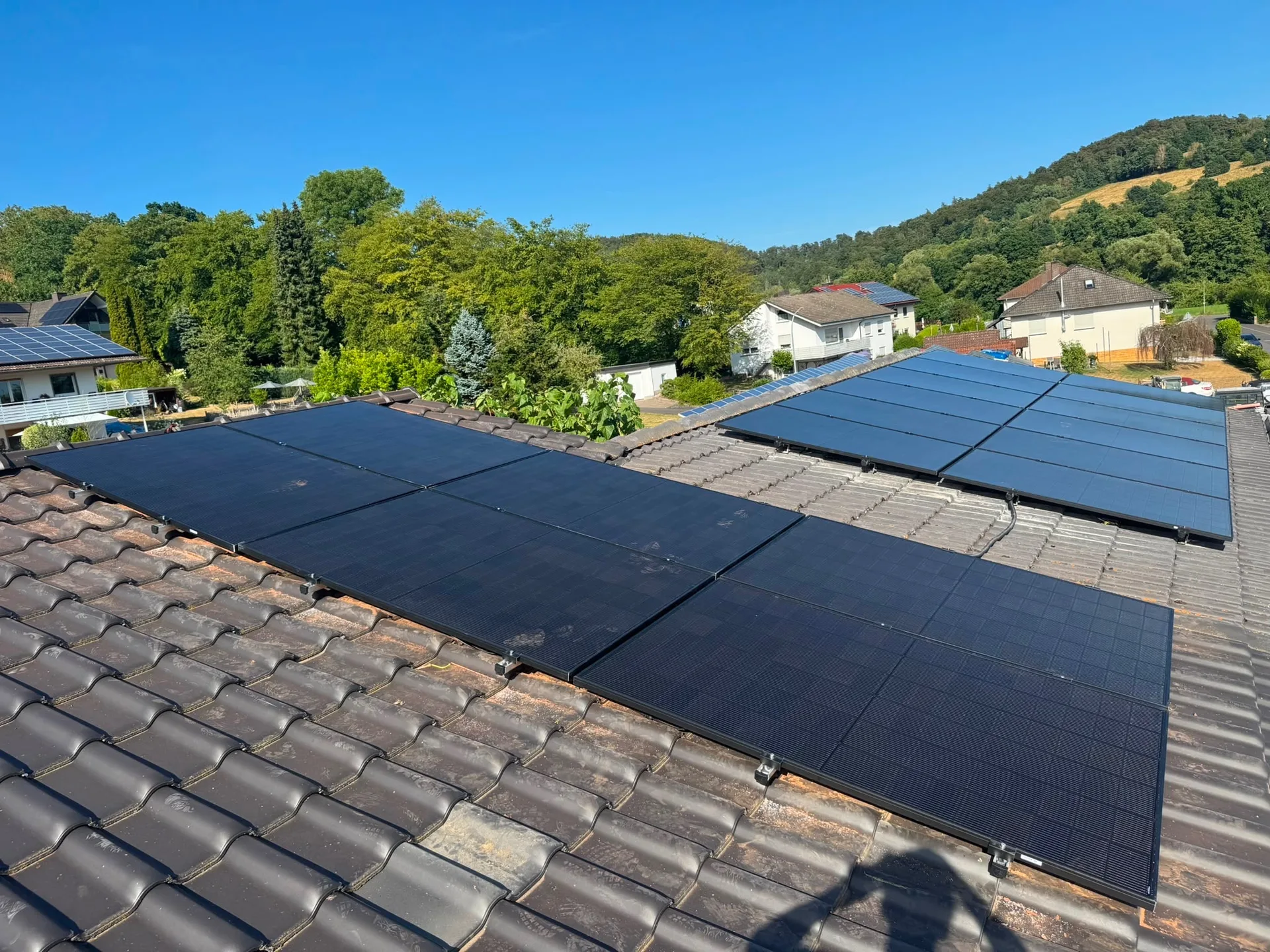 Schwarze Solarmodule auf einem Ziegeldach in Alheim-Heinebach, dahinter bewaldete Hänge